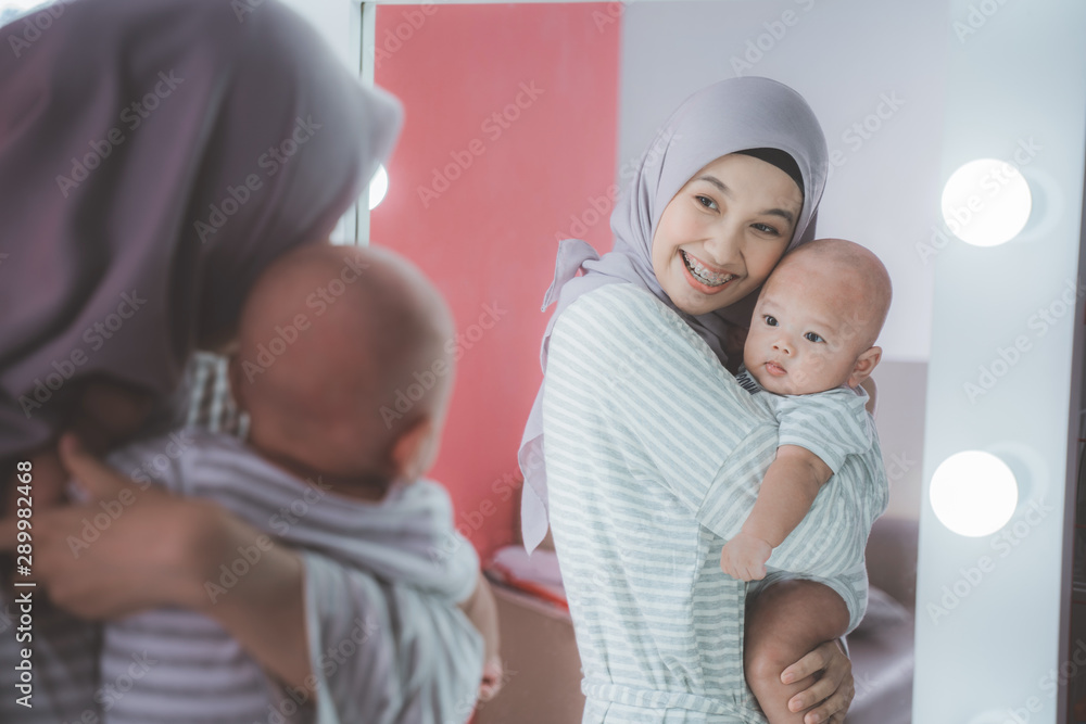 muslim woman with hijab playing with her baby looking at the mirror - obrazy, fototapety, plakaty 