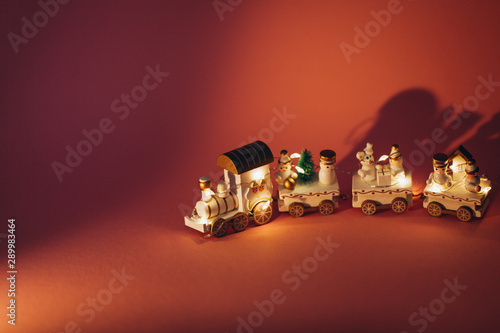 holiday magic concept. New Year. postcard. small toy miniature white train with Santa, snowman, garland lights. Christmas tree, on pink background in isolation. Copy space. Place text. 