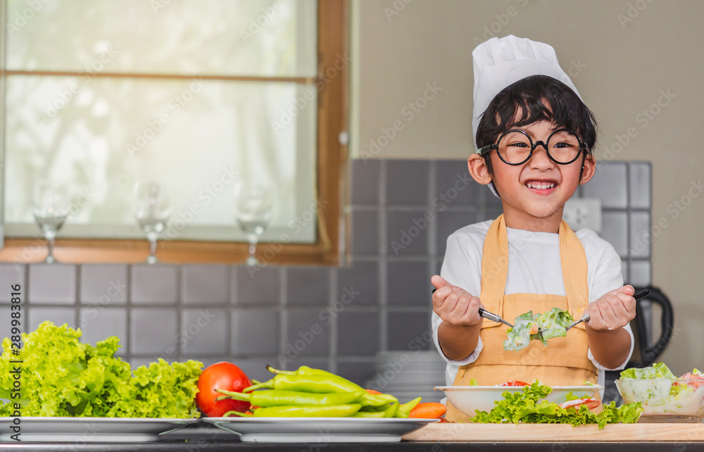 Asian Boy son cooking salad food holdind wooden spoon with vegetable holding tomatoes and carrots, bell peppers on plate for happy family cook food enjoyment lifestyle kitchen in home Asian Boy son cooking salad food holdind wooden spoon with vegetable holding tomatoes and carrots, bell peppers on plate for happy family cook food enjoyment lifestyle kitchen in home
