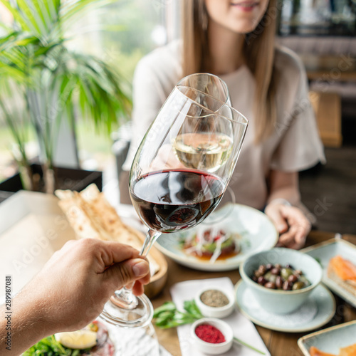 Date, man and woman Clink wine glasses. Beautiful young elegant woman in the restaurant with a wine glass. Dinner and a variety of dishes on the table. Italian cuisine