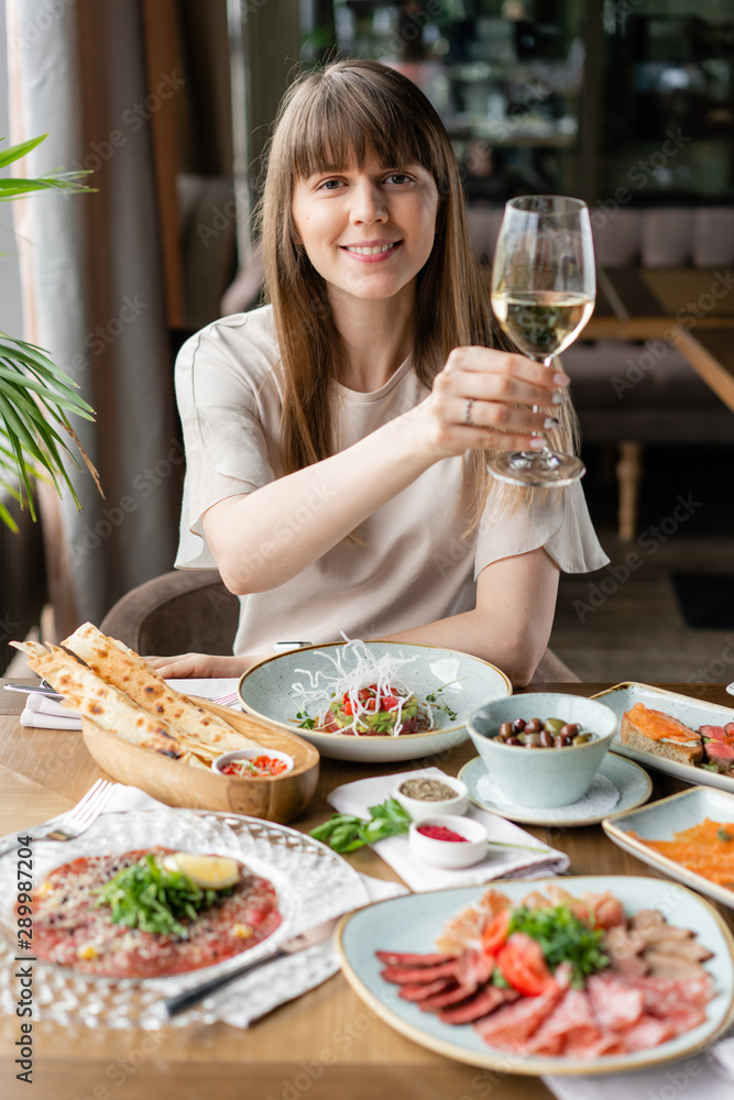 Portrait of a beautiful young elegant woman in the restaurant with a wine glass. Dinner and a variety of dishes on the table. Italian cuisine