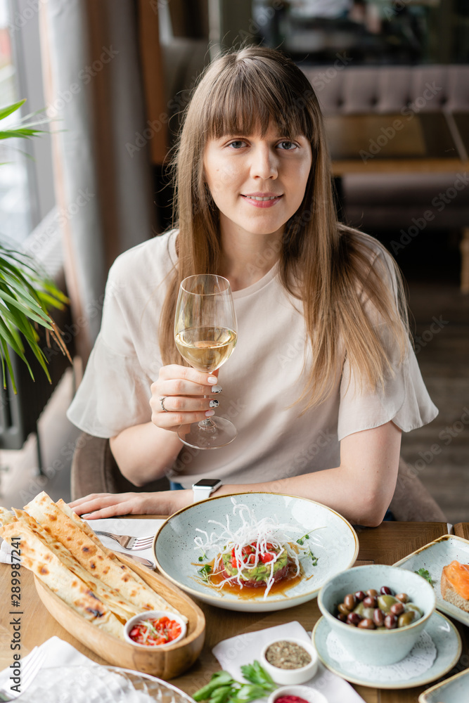 Portrait of a beautiful young elegant woman in the restaurant with a wine glass. Dinner and a variety of dishes on the table. Italian cuisine Portrait of a beautiful young elegant woman in the restaurant with a wine glass. Dinner and a variety of dishes on the table. Italian cuisine
