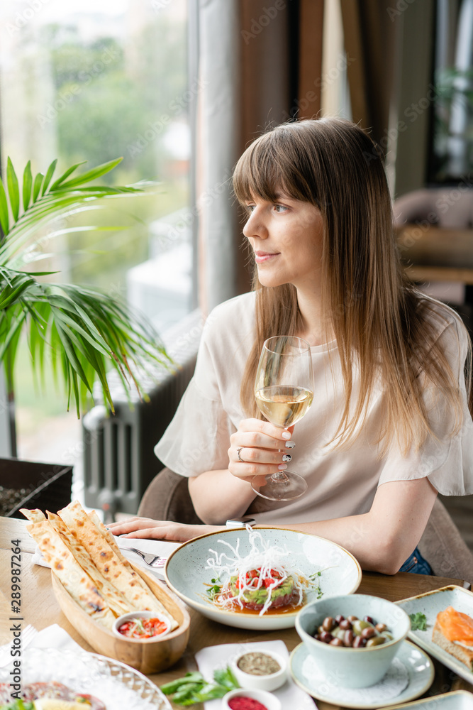 Portrait of a beautiful young elegant woman in the restaurant with a wine glass. Dinner and a variety of dishes on the table. Italian cuisine