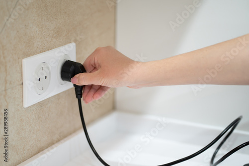 Close up Woman hand insert or pull out elecrticity plug in outlet on the wall photo