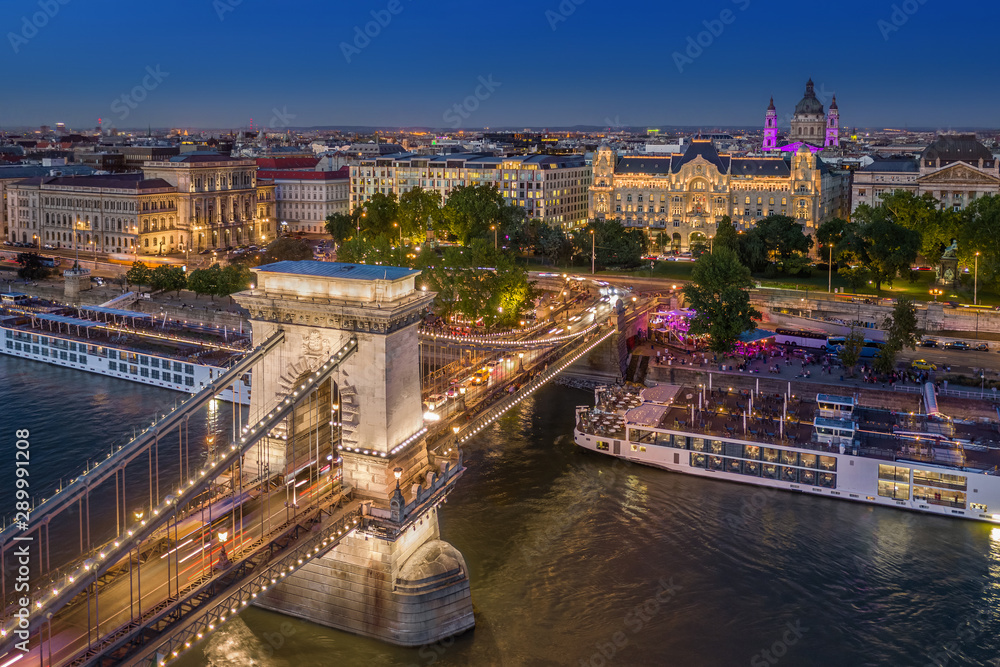 Budapest, Hungary - Aerial view of the beautiful illuminated Szechenyi Chain Bridge with St. Stephen's Basilica, Hungarian Academy of Sciences building and cruise ships at blue hour on a summer night