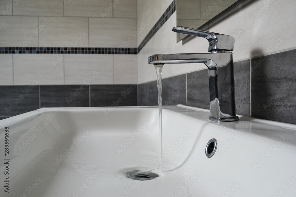 Open chrome faucet washbasin. A stream of water flows into the sink. Open chrome faucet washbasin. A stream of water flows into the sink.