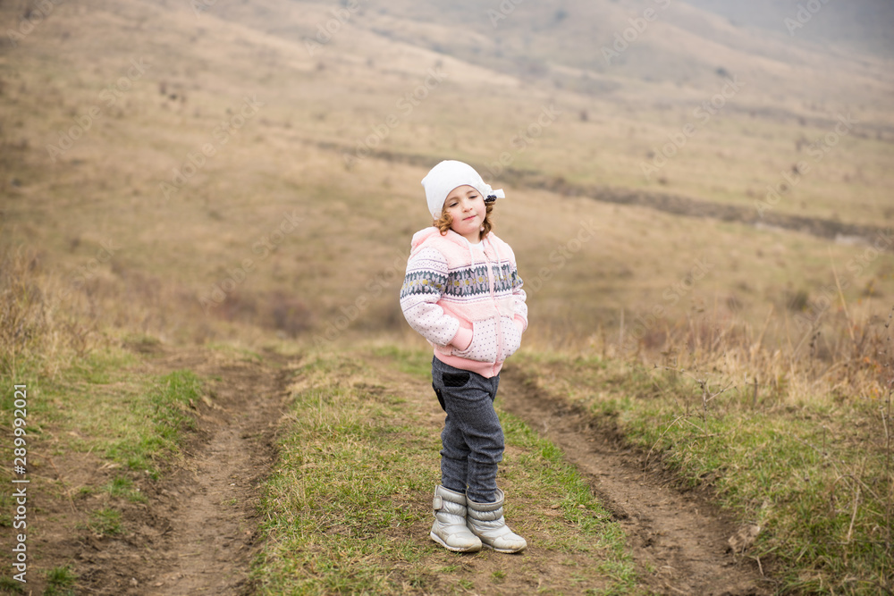 cute little girl in warm winter wool clothes on outdoor track in autumn mountains