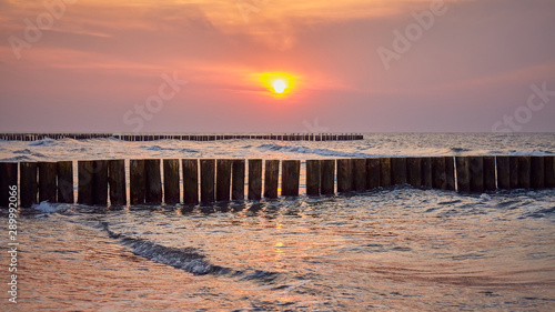 Wooden breakwater seen from a beach at sunset.