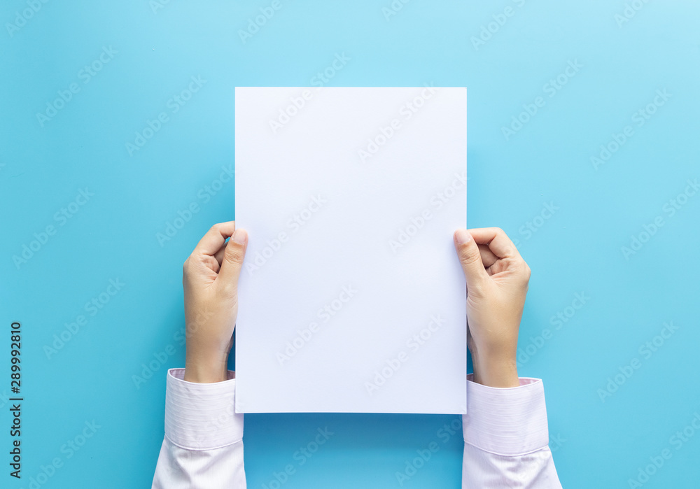 close up hands holding  empty white blank letter paper size A4 for flyer or invitation mock up isolated on a blue background. - obrazy, fototapety, plakaty 