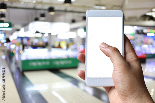 Hand of a man holding smartphone device in the Shopping mall background.