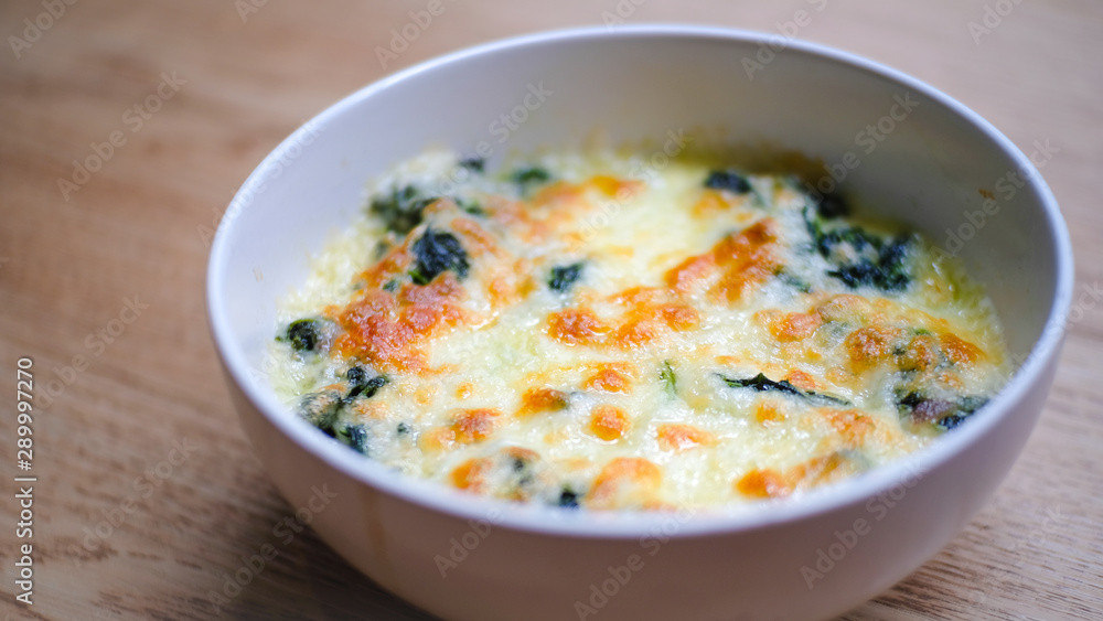 Baked Spinach with Cheese in white bowl on wooden table. food concept.