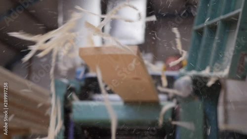 A solid wood plank coming out from an old planing machine. Slow motion shot of the plane tool processing wood while wood shavings are flying towards the camera. Shot taken in a woodworking workshop. photo