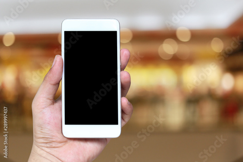 Hand of a man holding smartphone device in the blur Shopping mall background.