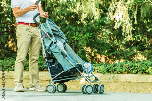 young father with smartphone waiting with baby cart in the park