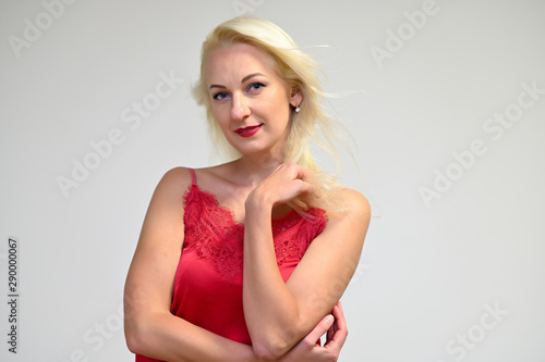 Concept portrait of a pretty young blonde woman with long beautiful hair in a red t-shirt on a white background in studio. Standing in front of the camera in various poses with a smile.