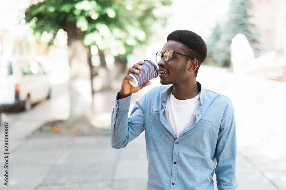 Portrait cool african man drinking coffee holding phone in hand standing on city street Portrait cool african man drinking coffee holding phone in hand standing on city street
