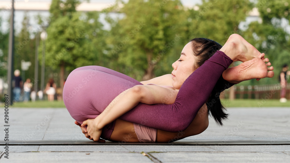 Side view of healthy women in sportswear practicing yoga outdoor. Ashtanga  Yoga pose Both Legs behind Head with eyes closed, working out wearing  sportswear pink top and pants, full length portrait. foto