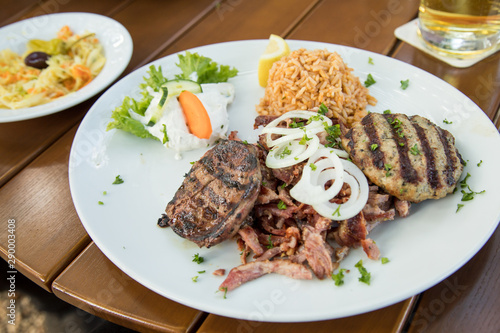 Griechischer Grillteller mit gegrillter Leber, Bifteki, Gyros, Zwiebeln, Tsatsiki, Krautsalat und Reis auf Holz Tisch
