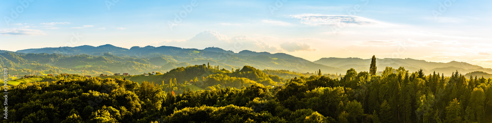 Naklejka premium Panoramiczny widok z winnicy na zielone wzgórza południowo-styryjskiego szlaku winiarskiego w Austrii o zachodzie słońca. Glanz an der Weinstrasse.