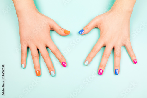 Woman's hands with perfect manicure in trendy neon colors on turquoise background. Beauty concept.