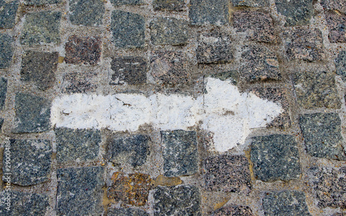 A rightwards arrow painted with white paint on the old stoneblock pavement cobbled with square granite blocks photo