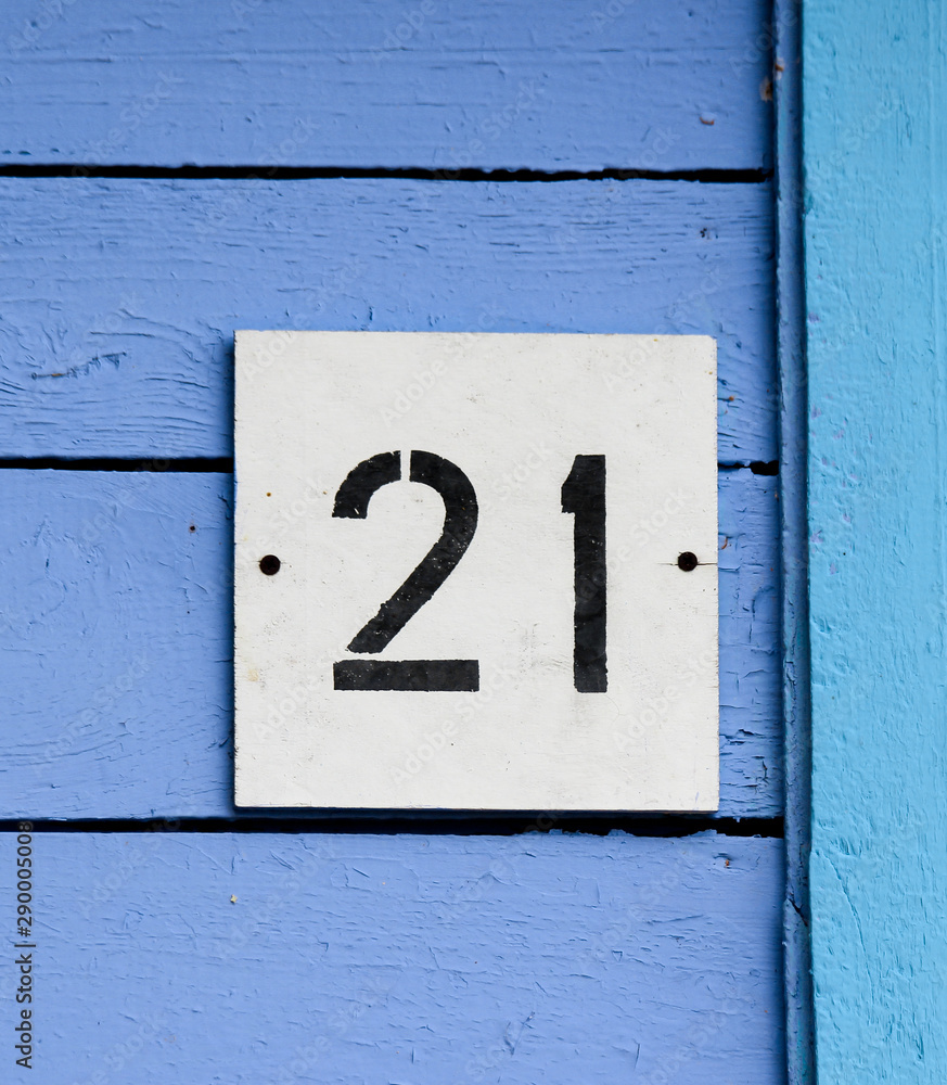 Arabic figure 21 (twenty one) painted with black on a white square plate affixed on an old wooden wall covered with blue paint