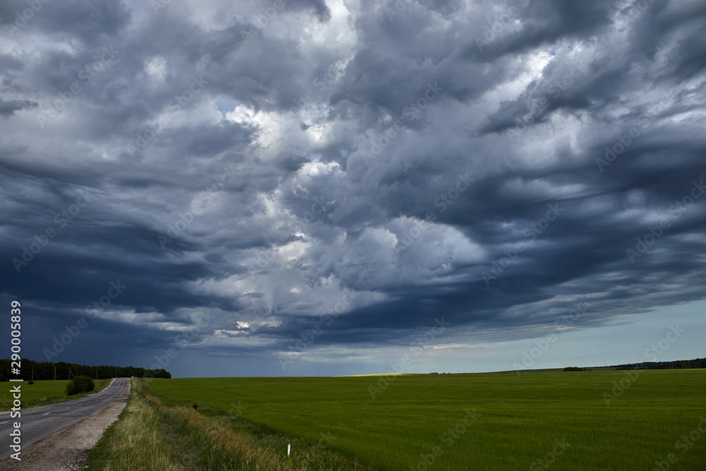 country road along the field under heavy clouds