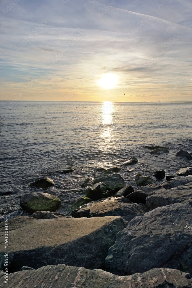 Wavy seascape view at sunset from the shore with large mossy stones and sea birds over the water surface.