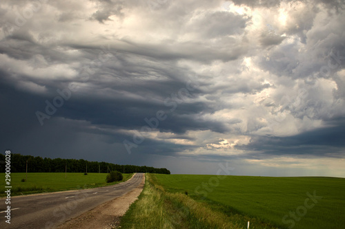country road along the field under heavy clouds