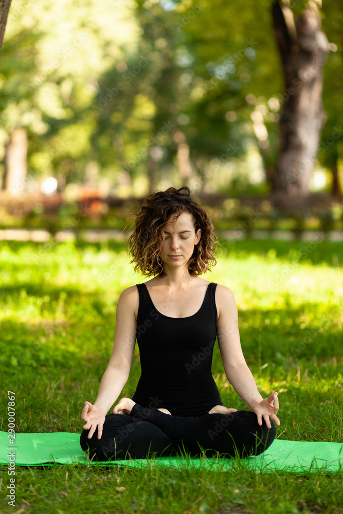Attractive and peaceful woman sitting in yoga lotus position in the morning in park. Meditation, concentration and relaxation. Attractive and peaceful woman sitting in yoga lotus position in the morning in park. Meditation, concentration and relaxation.