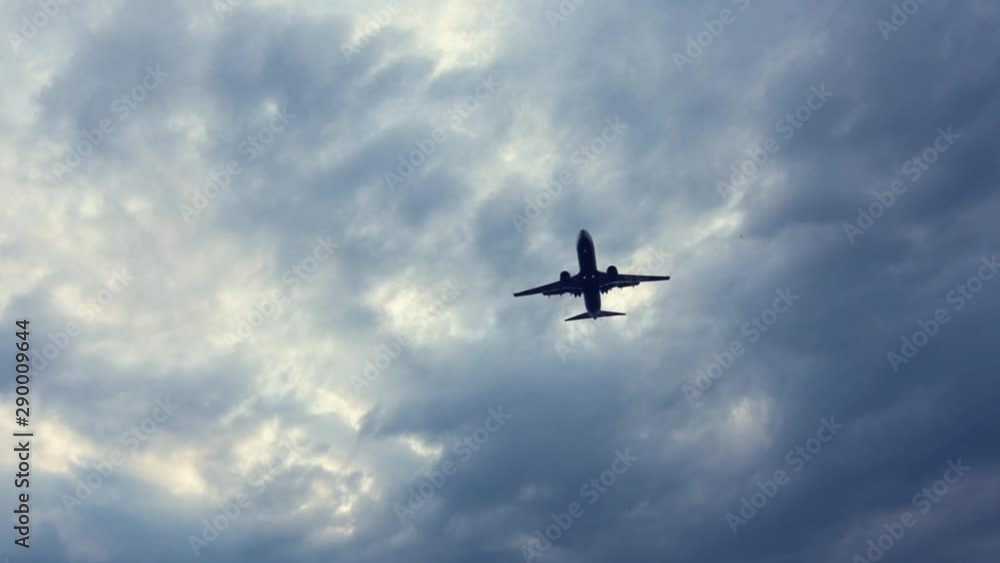 Commercial passenger airplane flying close overhead against cloudy stormy sky Commercial passenger airplane flying close overhead against cloudy stormy sky