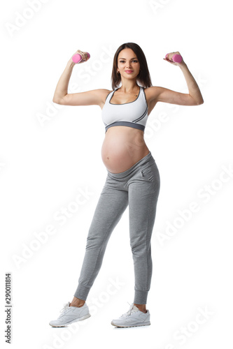 Slender athletic pregnant girl is engaged in fitness with dumbbells standing in full length isolated on white background.