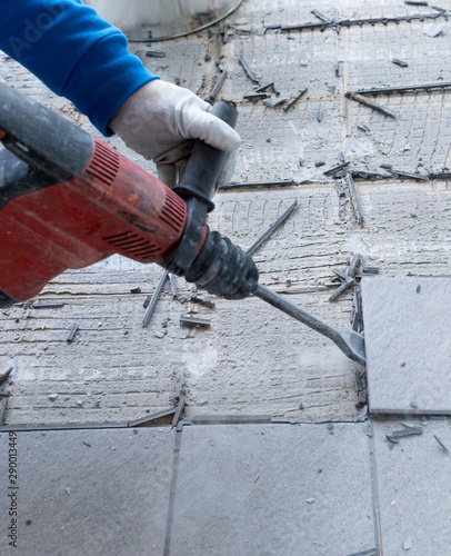 construction worker using a handheld demolition hammer and wall breaker to chip away and remove old floor tiles during renovation work