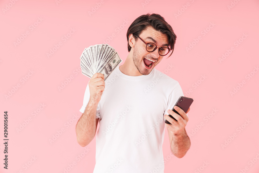 Image of amazed happy man wearing eyeglasses holding cash money and using cellphone Image of amazed happy man wearing eyeglasses holding cash money and using cellphone