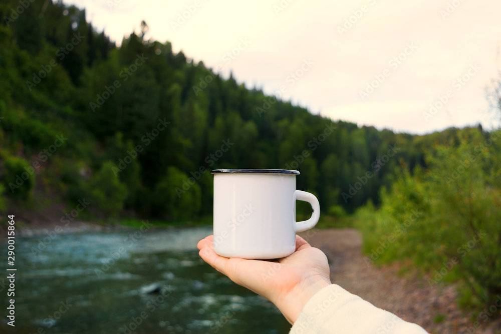 Woman holding enamel mug with riverside view Woman holding enamel mug with riverside view