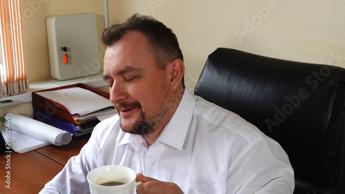 Young man the director of the company sits in the office and drinks coffee