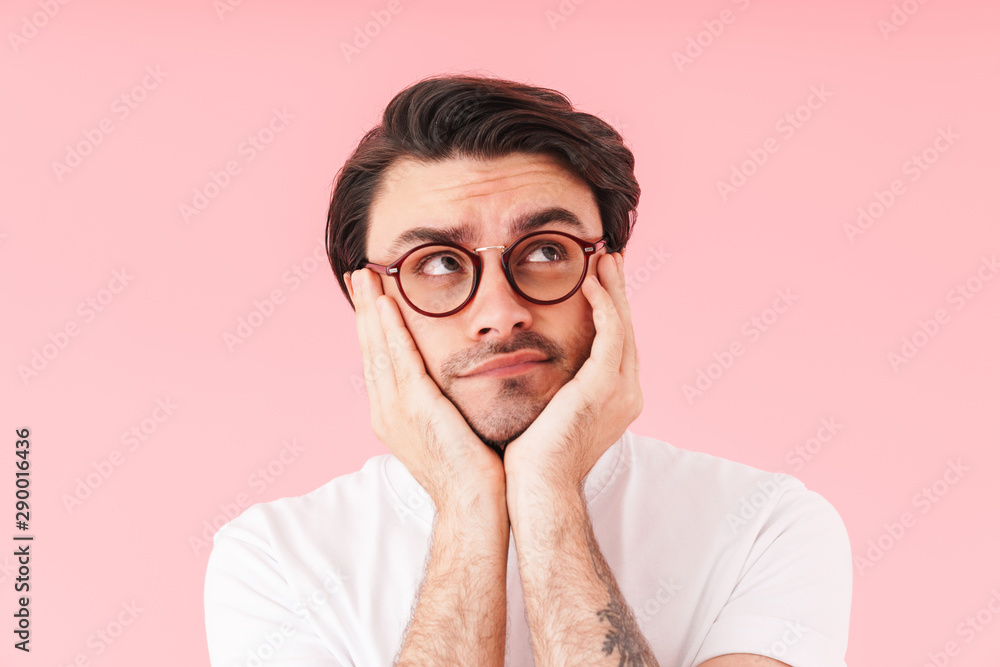 Image of brunette brooding man wearing eyeglasses looking upward at copyspace and propping his head Image of brunette brooding man wearing eyeglasses looking upward at copyspace and propping his head