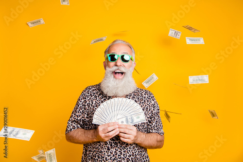 Photo of elderly old confident rich man holding banknotes in his hands and being rained with currency while isolated with yellow background photo