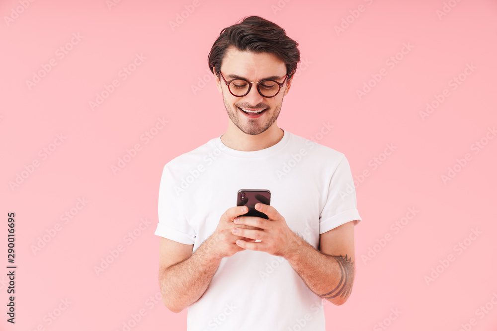 Image of unshaven happy man wearing eyeglasses smiling and typing on cellphone Image of unshaven happy man wearing eyeglasses smiling and typing on cellphone