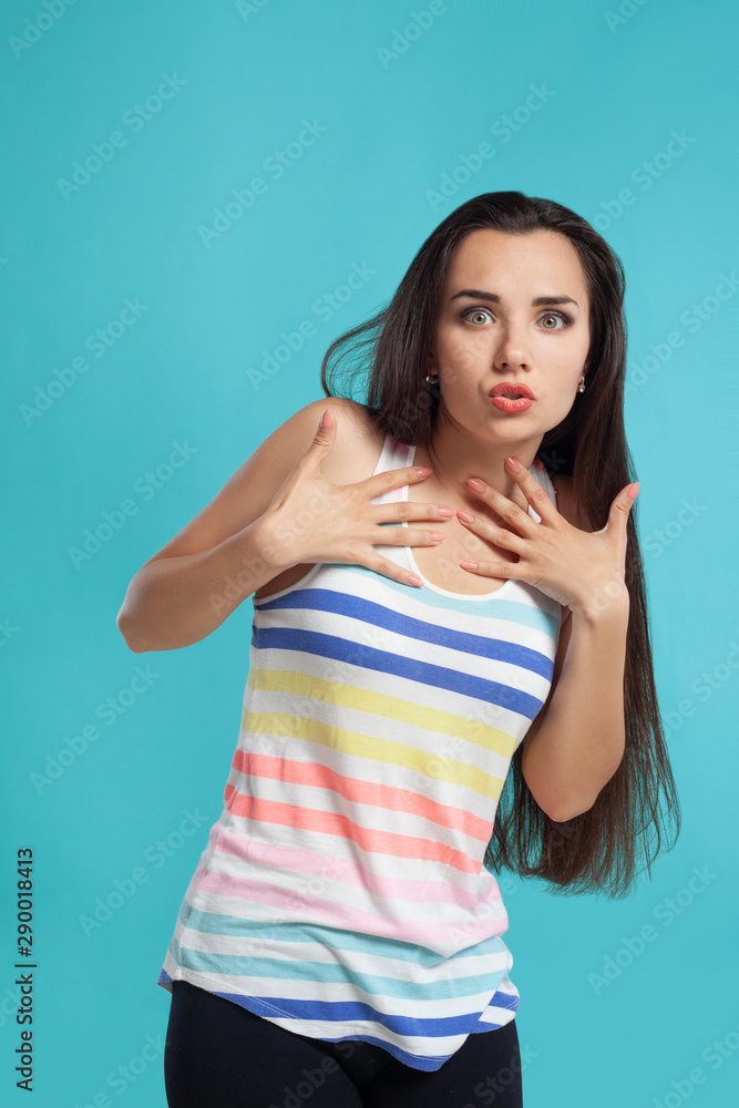Brunette woman with long hair, dressed in striped shirt and black leggings, posing against blue studio background. Sincere emotions. Close-up. Brunette woman with long hair, dressed in striped shirt and black leggings, posing against blue studio background. Sincere emotions. Close-up.