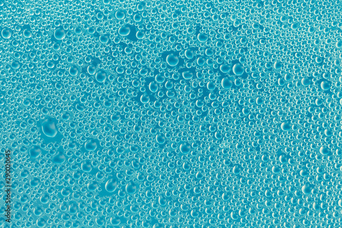 Water drops on blue glass surface. Abstract bubbles background. Glossy shiny texture. Drops pattern. Transparent condensation. Modern art backdrop for design.