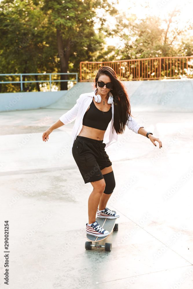 Photo of attractive young woman wearing headphones riding skateboard in skate park Photo of attractive young woman wearing headphones riding skateboard in skate park