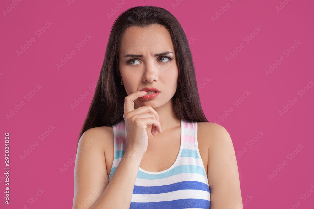 Brunette woman with long hair, dressed in colorful striped shirt, posing against pink studio background. Sincere emotions. Close-up. Brunette woman with long hair, dressed in colorful striped shirt, posing against pink studio background. Sincere emotions. Close-up.