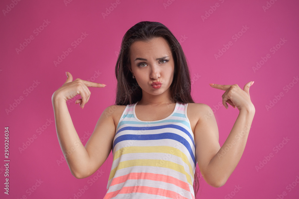 Brunette woman with long hair, dressed in colorful striped shirt, posing against pink studio background. Sincere emotions. Close-up. Brunette woman with long hair, dressed in colorful striped shirt, posing against pink studio background. Sincere emotions. Close-up.