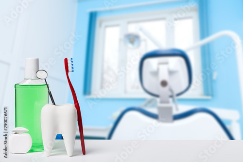 Dental health and teethcare concept. Dental mirror in white tooth model near mouthwash  toothbrush and dental floss against dental office and chair background