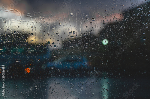 Raindrops on a car glass against a blurred background with a view of the city and the lights of cars.