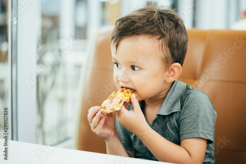 a little boy in a cafe or pizzeria sitting on the couch at the table and eats a piece of cut pizza  very tasty