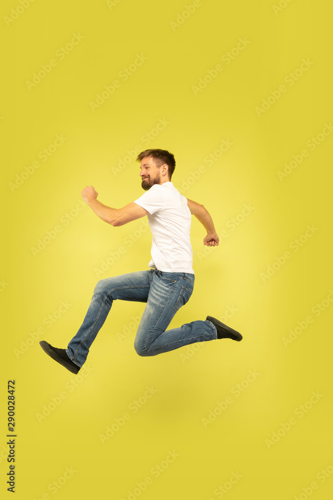 Full length portrait of happy jumping man isolated on yellow background. Caucasian male model in casual clothes. Freedom of choices, inspiration, human emotions concept. Running happy. Full length portrait of happy jumping man isolated on yellow background. Caucasian male model in casual clothes. Freedom of choices, inspiration, human emotions concept. Running happy.