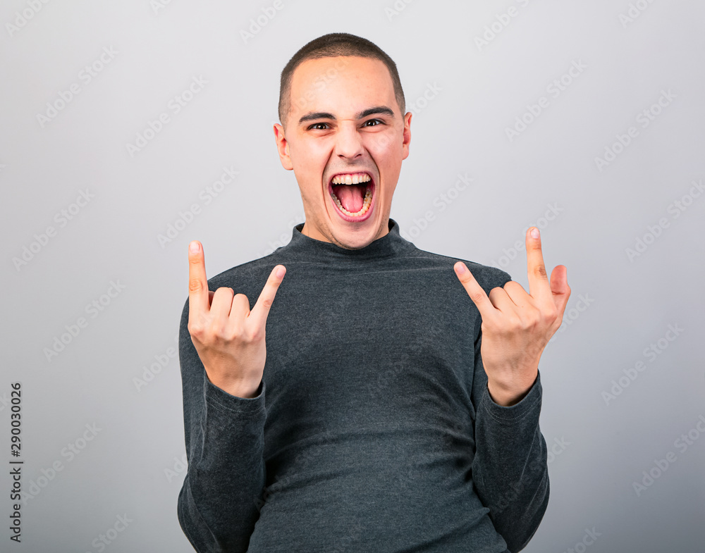Crazy grimacing man showing the rock sign by two hands with crying open mouth on blue background with empty copy space. Closeup Crazy grimacing man showing the rock sign by two hands with crying open mouth on blue background with empty copy space. Closeup