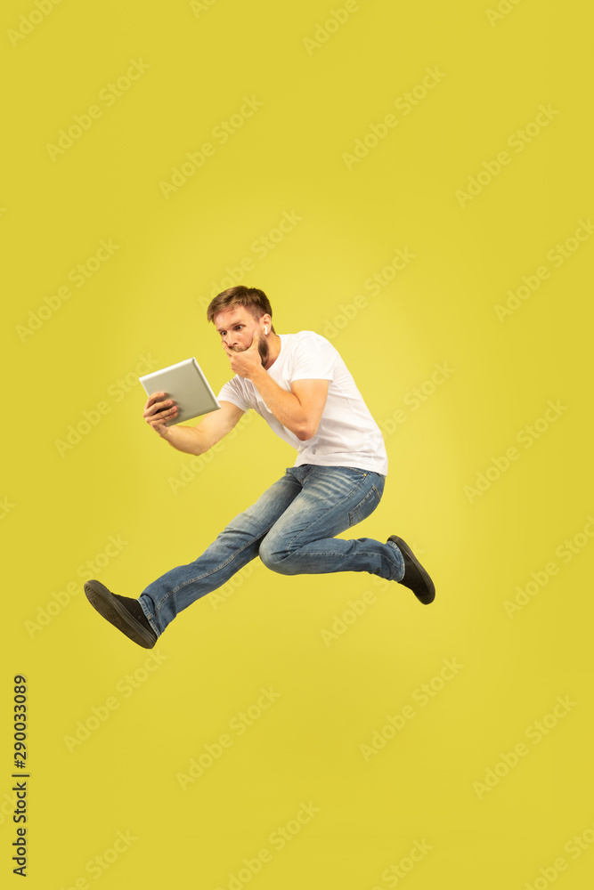 Full length portrait of happy jumping man isolated on yellow background. Caucasian male model in casual clothes. Freedom of choices, inspiration, human emotions concept. Takes video for vlog or Full length portrait of happy jumping man isolated on yellow background. Caucasian male model in casual clothes. Freedom of choices, inspiration, human emotions concept. Takes video for vlog or